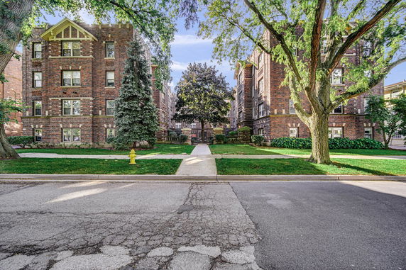 Front view of two brick multi-story residential buildings with a central walkway and trees.