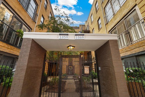 Front view of a multi-story apartment building entrance with gate and signage.