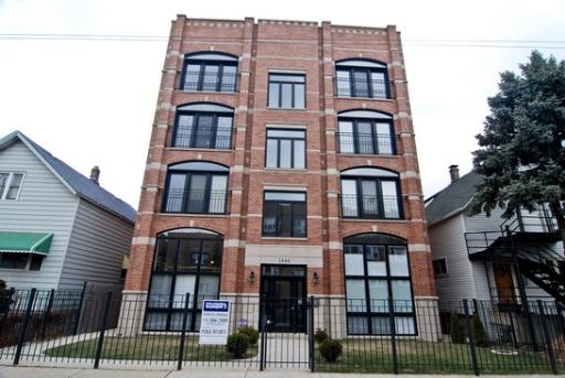 Front view of a four-story brick apartment building with large windows and a gated entrance.