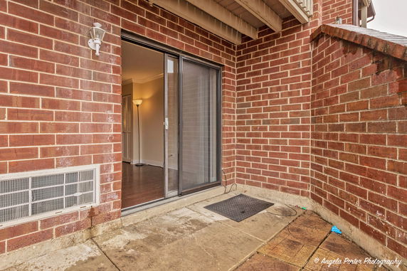 View of a brick-walled outdoor patio area with a sliding glass door and an exterior light fixture.
