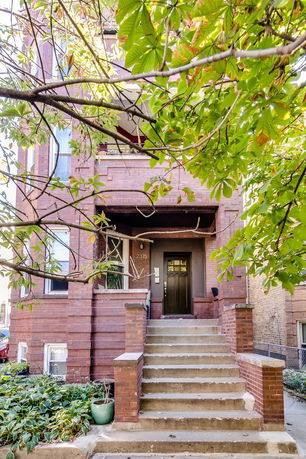 Front view of a multi-story brick house with steps leading to the entrance.