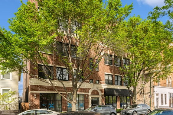 Front view of a multi-story brick building with large trees in front.