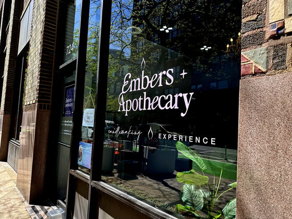 Street view of a storefront with large glass windows displaying the name 'Embers + Apothecary.'