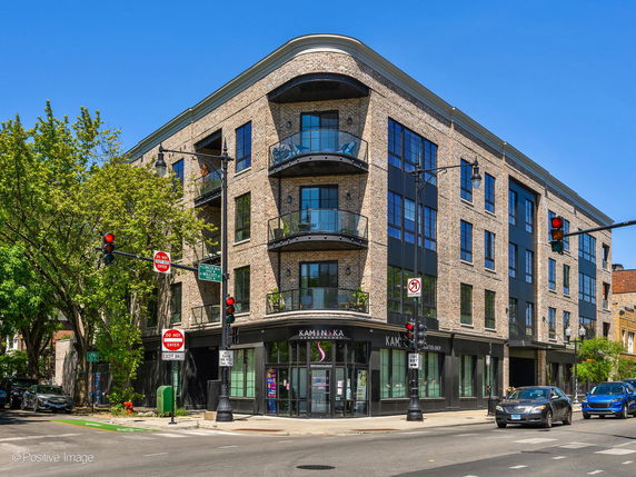 Front view of a multi-story building with large windows and balconies located at a street intersection.