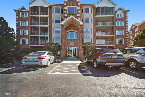 Front view of a multi-story building with brick facade and parked cars in front.
