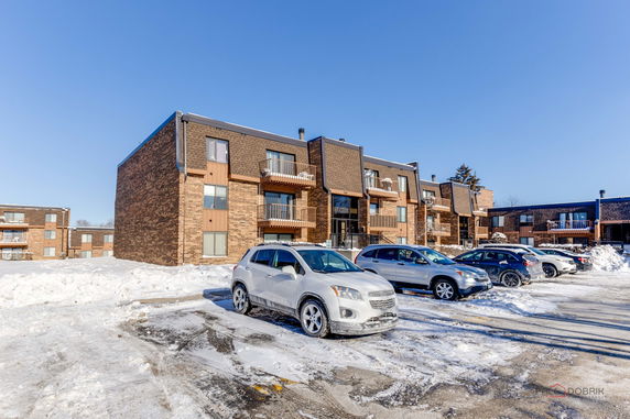 Front view of a multi-story apartment building with balconies and a parking area in front.