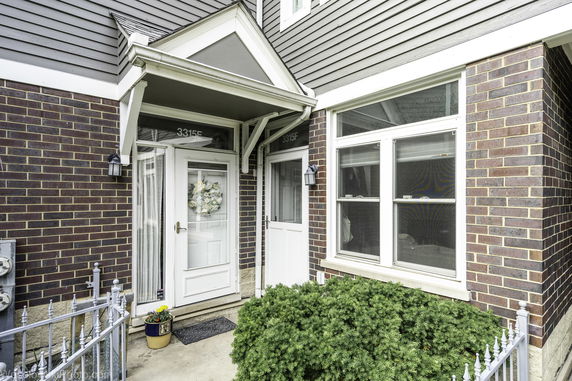 Front view of a brick residential building entrance with a small porch and decorative wreath on the door.