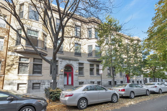 Front view of a multi-story residential building with a red entrance door and parked cars.