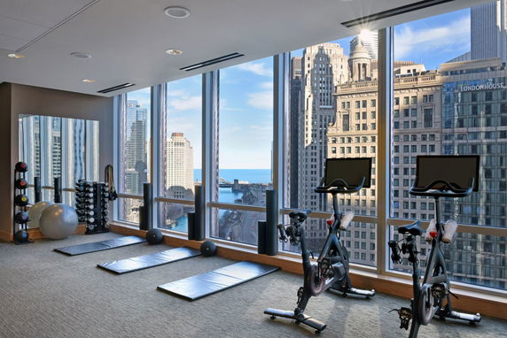 Indoor gym area with exercise equipment, large windows offering a view of city buildings.
