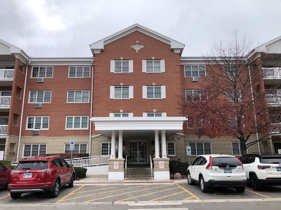 Front view of a multi-story residential building with a central entrance and parking area.