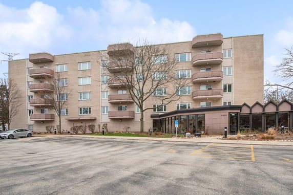 Front view of a multi-story apartment building with balconies and a parking area.