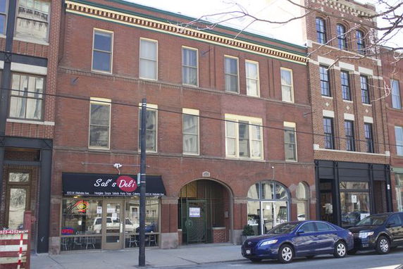 Front view of a three-story brick building with a deli on the ground floor.
