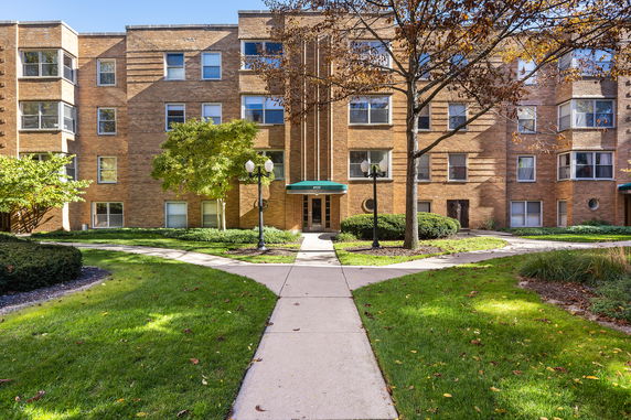 Front view of a multi-story brick apartment building with a central entryway and landscaping.
