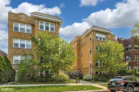 Front view of a multi-story apartment building with a brick facade and a tiled roof.