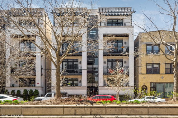 Front view of a multi-story apartment building with balconies and large windows.