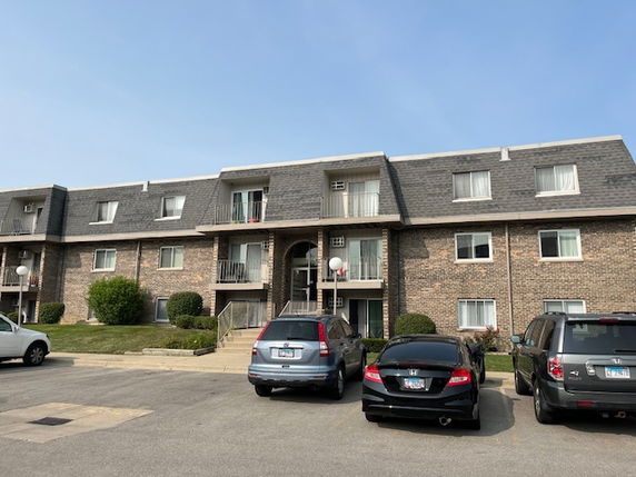 Front view of a multi-story apartment building with brick exterior and parking area.
