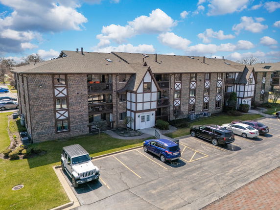 Front view of a multi-story brick building with Tudor-style accents and a parking area.