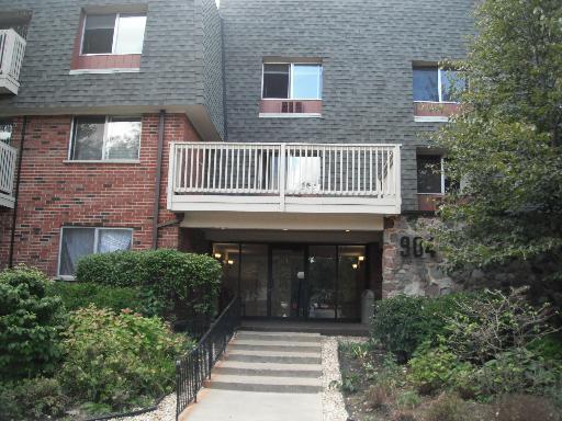 Front view of a multi-story residential building with a balcony and entrance stairs.