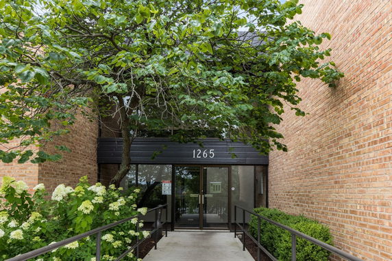 Front view of a brick building entrance with a glass door and a canopy labeled 1265.