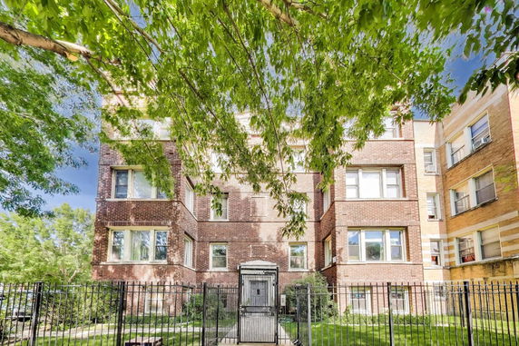 Front view of a multi-story brick apartment building with a gated entrance.
