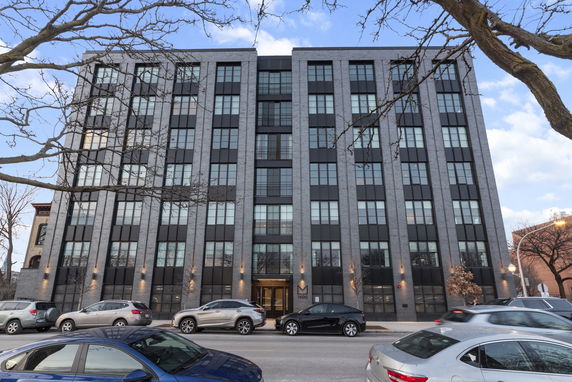 Front view of a multi-story apartment building with large windows and cars parked on the street.