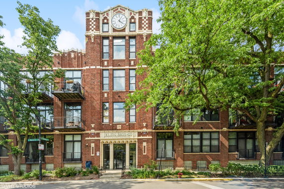 Front view of a multi-story brick building with a clock at the top and large windows.