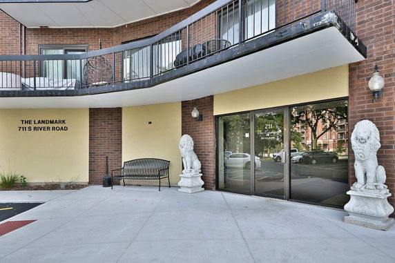 Front view of a building entrance with glass doors, lion statues, and a balcony above.