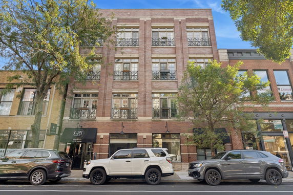Front view of a multi-story brick building with balconies and street-level shops.
