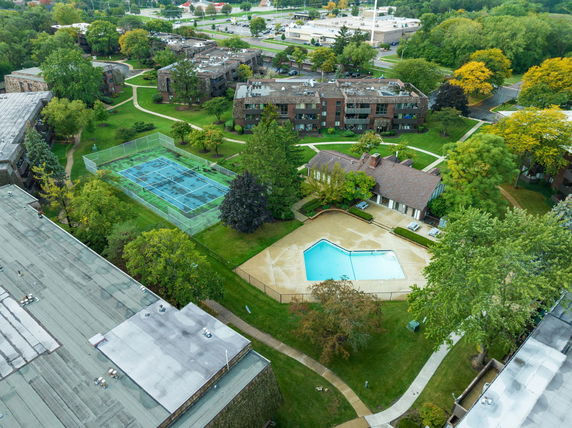 Aerial view of a residential complex with a swimming pool, tennis court, and surrounding greenery.