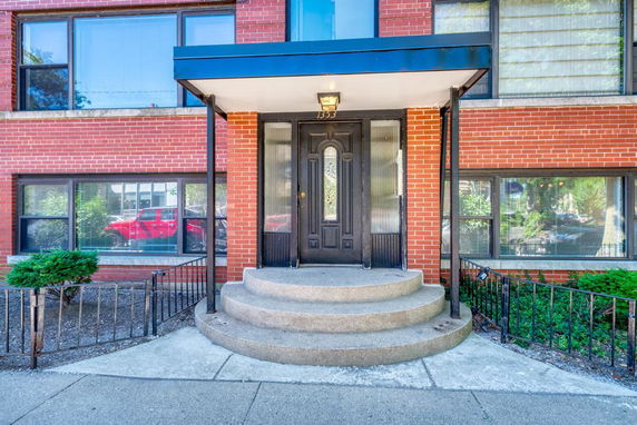 Front view of a brick apartment building entrance with steps and a covered canopy.