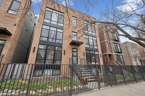 Front view of a modern three-story brick apartment building with large windows and a gated entry.