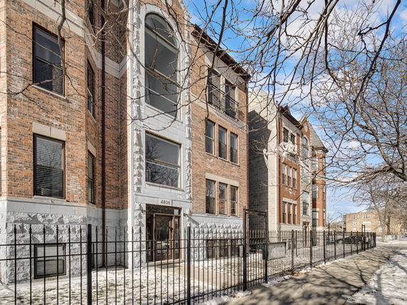 Front view of a multi-story brick residential building with large windows and a gated entrance.