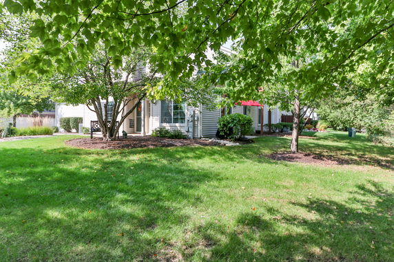 Front view of a house with tan siding and a small porch, surrounded by trees and grass.