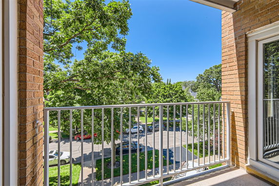 View from a balcony overlooking a street with trees and parked cars.
