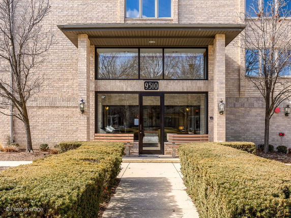 Front view of a multi-story brick building with glass entrance and number 9510.