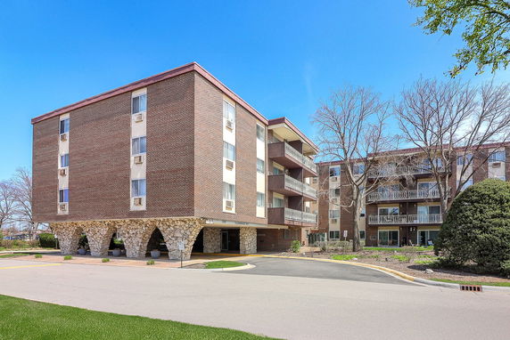 Front view of a multi-story brick apartment building with balconies and unique stone arch supports.