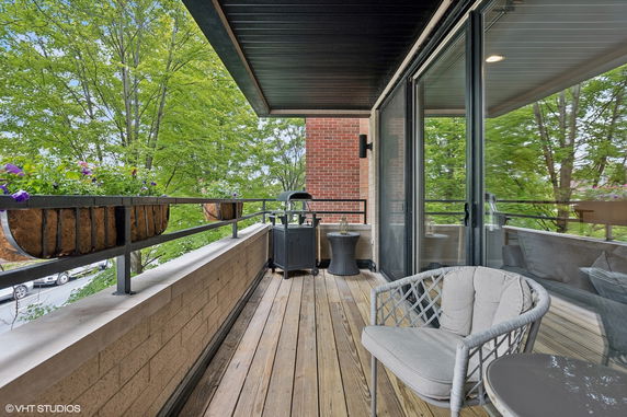 Outdoor balcony with seating area and railing-mounted planters, surrounded by trees.