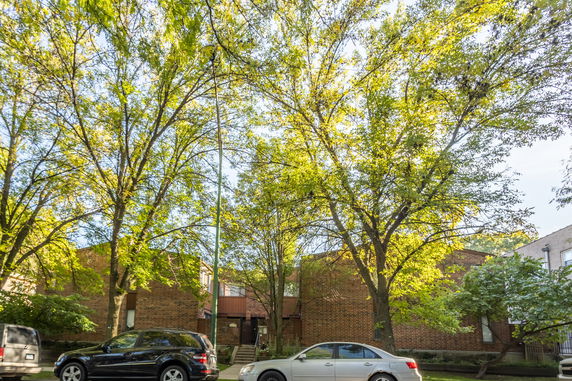 Front view of a brick building with trees and parked cars in front.