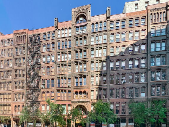 Front view of a multi-story brick building with many windows and a fire escape ladder.