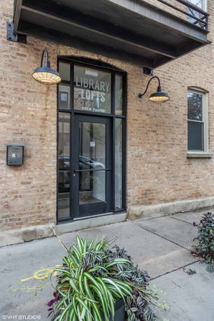 Front view of a brick building entrance with a glass door and two wall-mounted lamps.