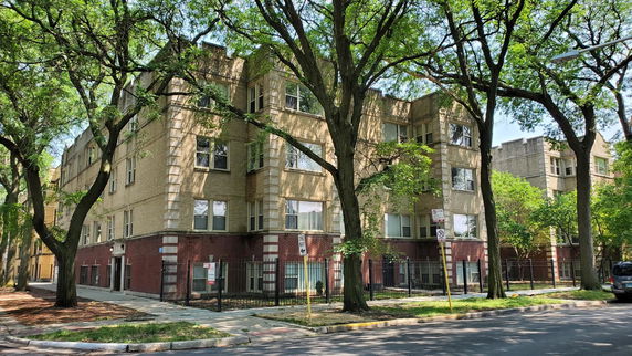 Front view of a multi-story residential building with trees and street in foreground.