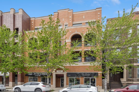 Front view of a multi-story brick building with arched balconies and retail spaces at ground level.