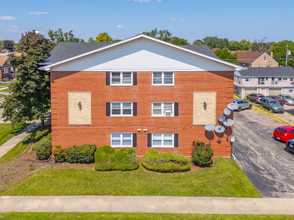 Front view of a brick multi-story residential building with several satellite dishes on the side wall.