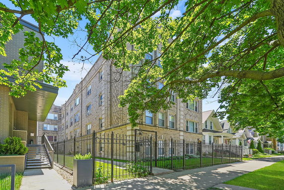 Front view of a multi-story apartment building with brick exterior and fenced entrance.