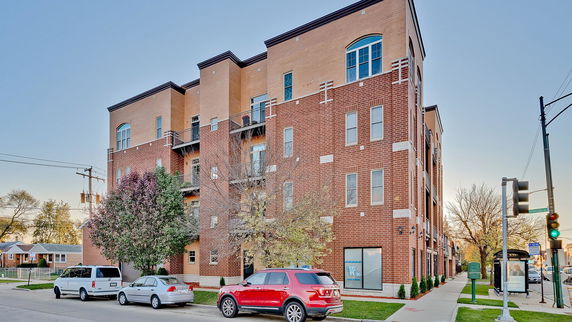 Front view of a multi-story brick apartment building with parking in front.