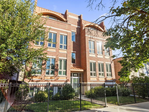 Front view of a multi-story brick building with several windows and a gated entrance.