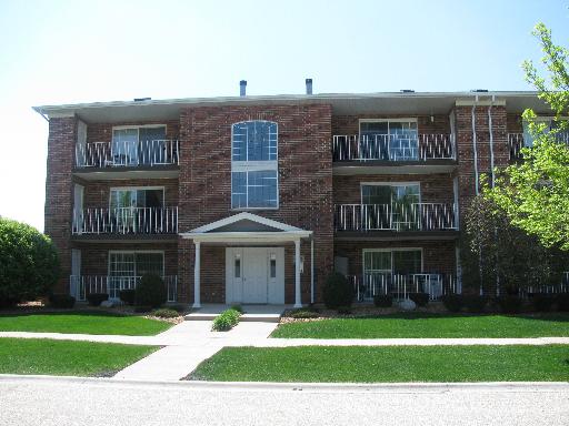 Front view of a three-story brick apartment building with balconies.