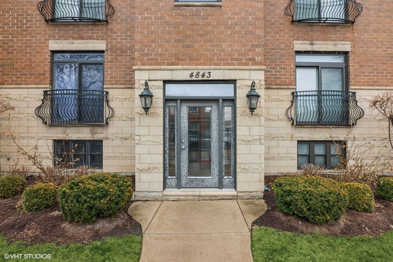 Front view of a brick building entrance with decorative railings and outdoor lighting.