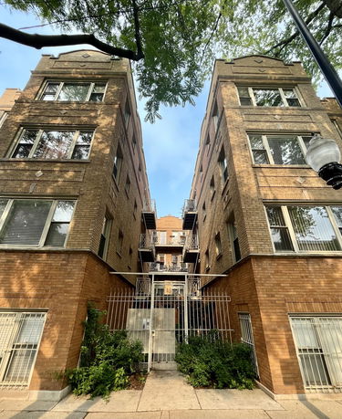 Front view of a brick apartment building with multiple balconies and gated entrance.