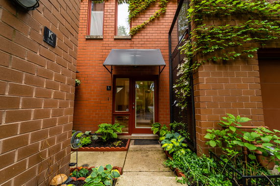 Front view of a brick building entrance with a metal awning and surrounding plants.